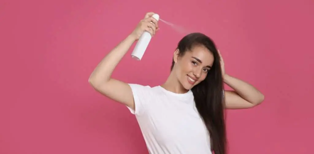 Woman using too much spray product on pink background